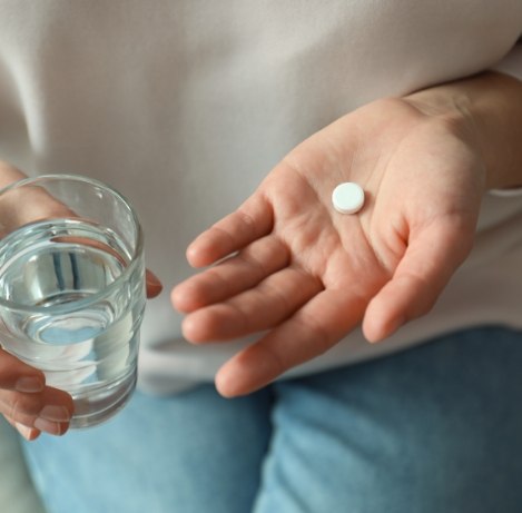 Person holding a white pill and a glass of water